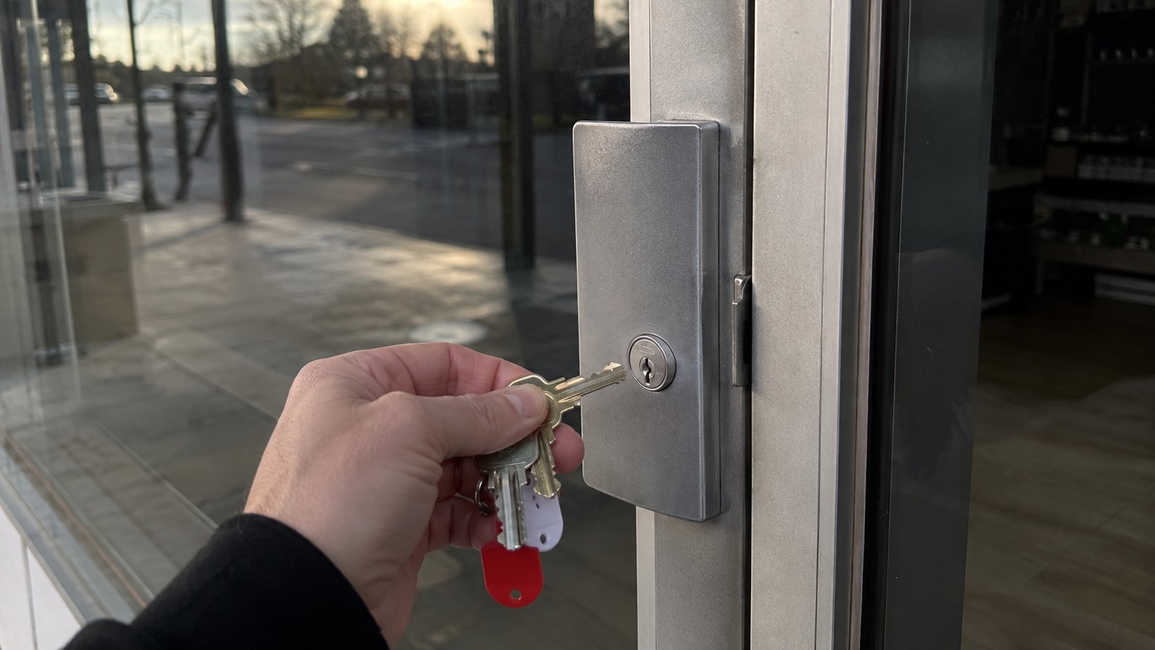 A commercial glass door at night with locksmith tools in the deadlatch