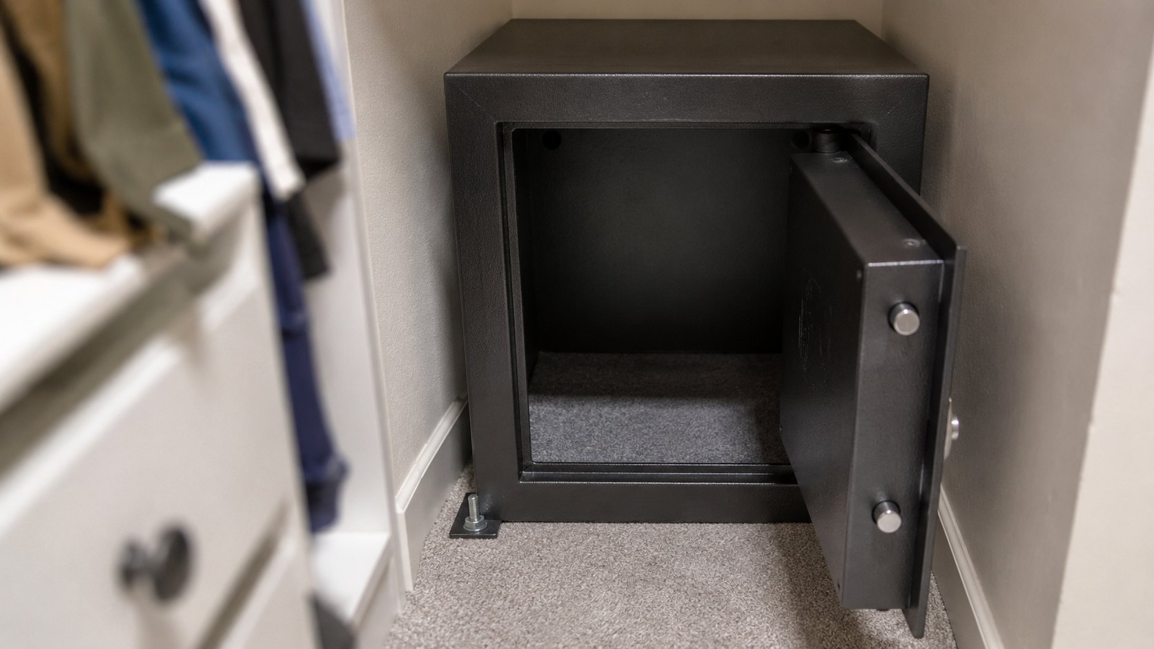 A home safe anchored in the corner of a wardrobe with its door open