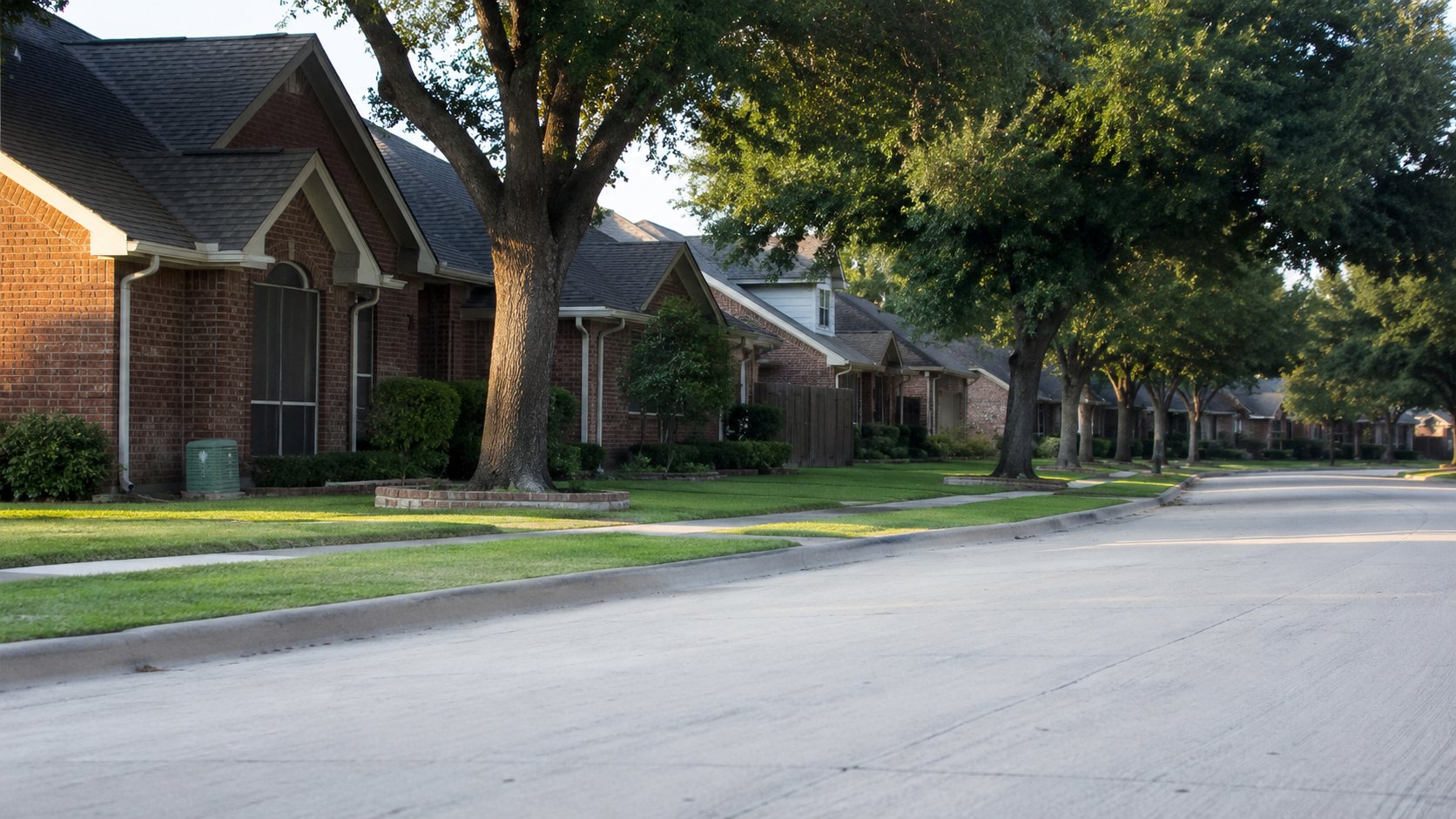 A quiet residential street of brick houses in North Texas in late afternoon light