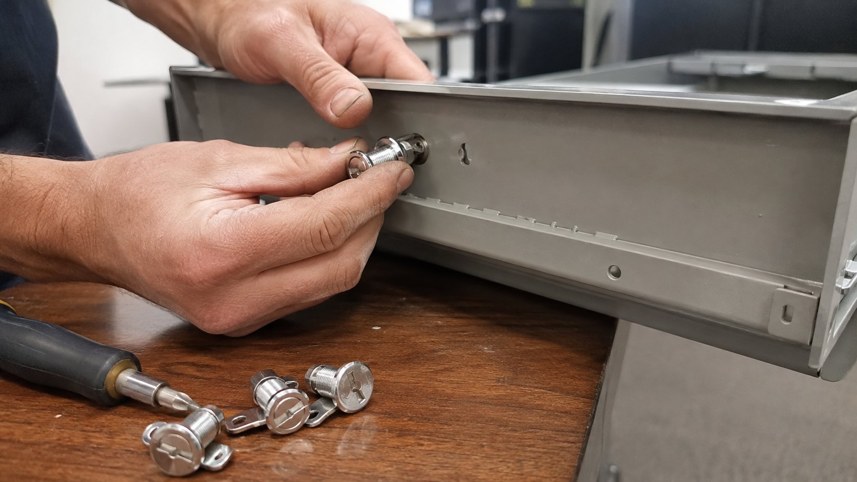 A small cam lock being fitted to an office filing cabinet drawer