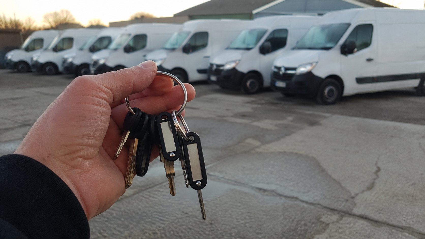 A row of white work vans at first light with a bunch of numbered fleet keys held up