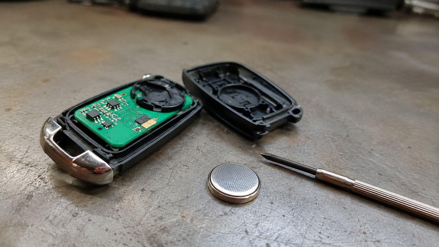 A car key fob opened on a bench showing its board and a replacement coin cell