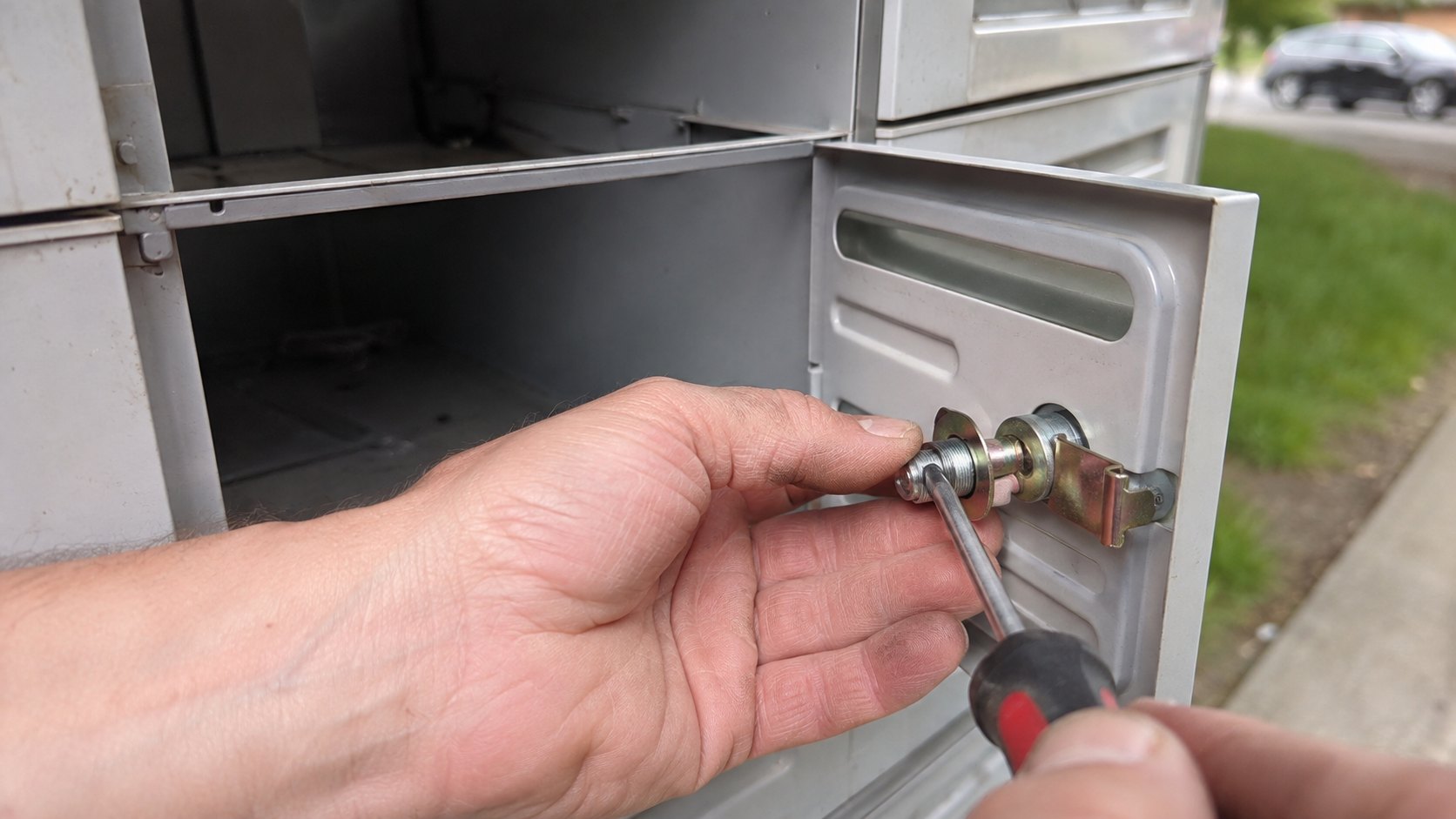 A cluster mailbox with one door open, its cam lock being replaced