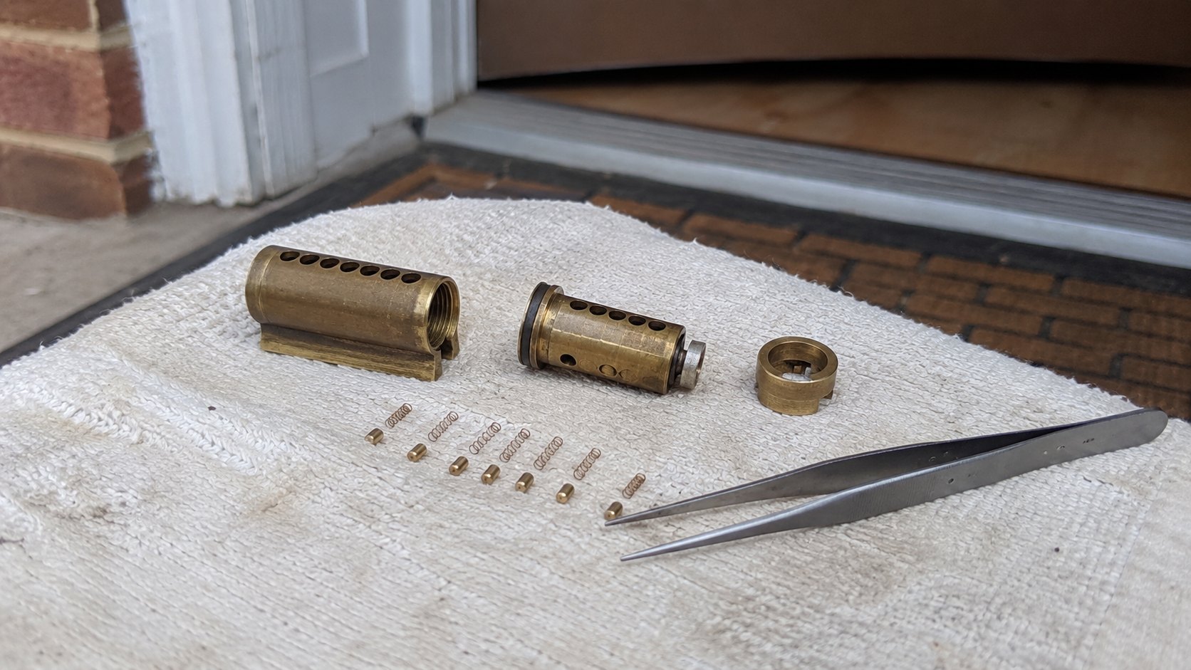 A pin tumbler lock cylinder opened on a work cloth with its brass pins laid out for rekeying