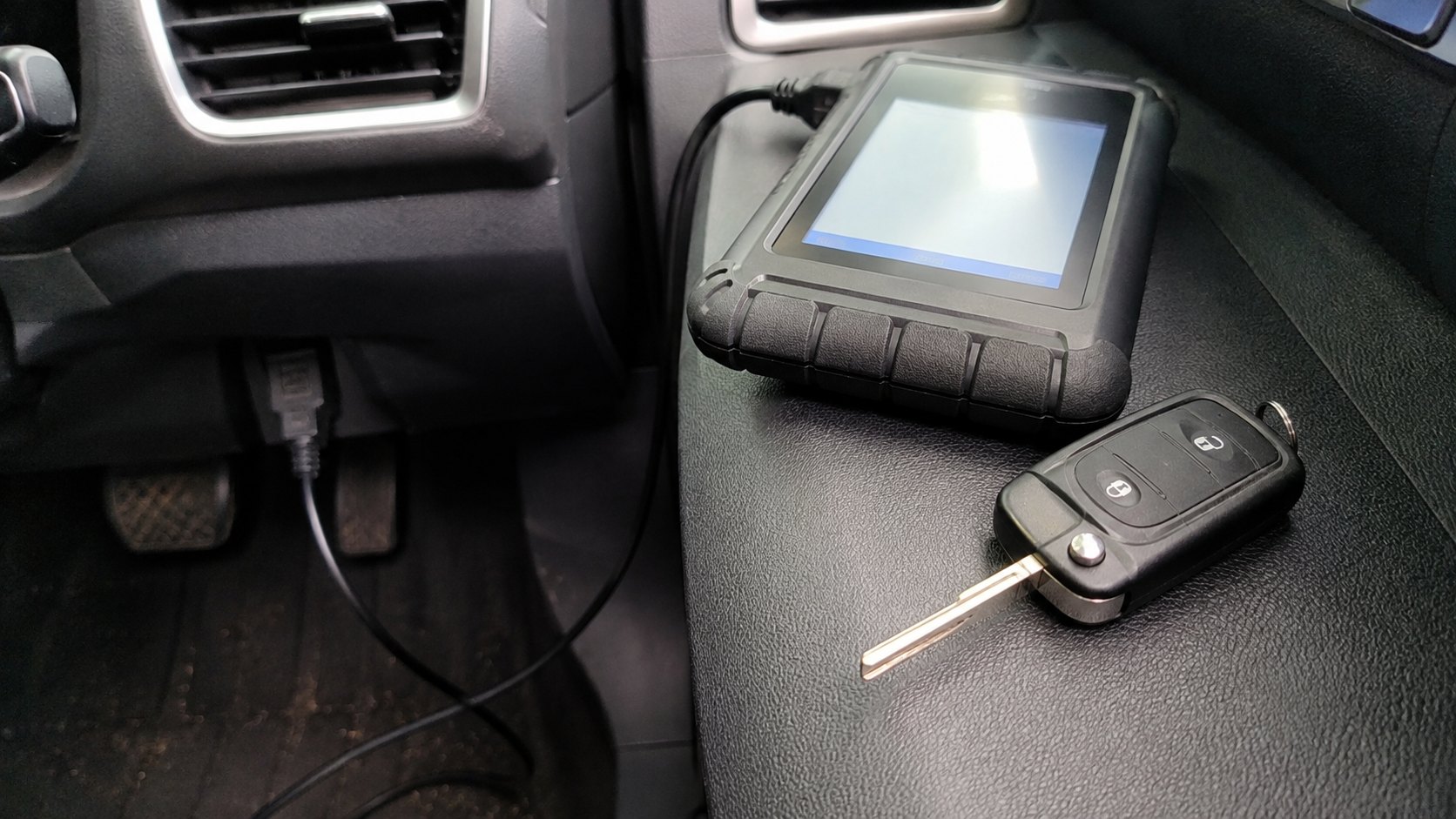 A transponder car key beside a lit diagnostic programmer connected to the OBD port